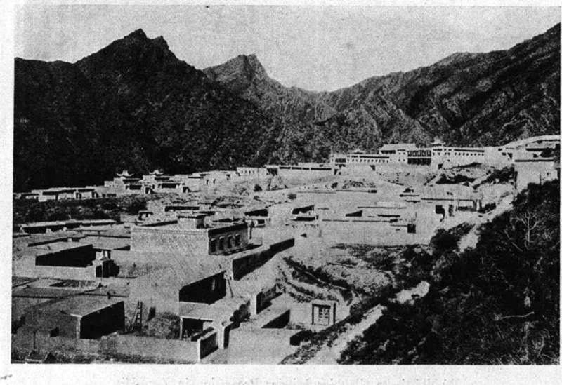 Photograph of a Mongolian monastery of flat-roofed buildings below a rock ridge